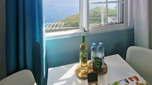 Une pièce avec une fenêtre donnant sur la mer, une table avec une bouteille et des verres, et une chaise.