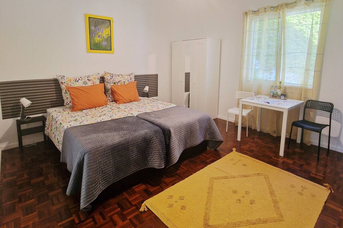 A bedroom with a bed, a desk, a chair, a wardrobe, a lamp, and a painting on the wall.