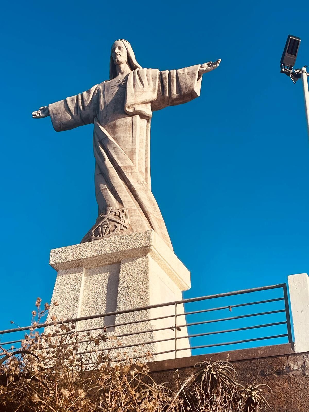 Una statua con le braccia aperte, sullo sfondo di un cielo azzurro intenso.