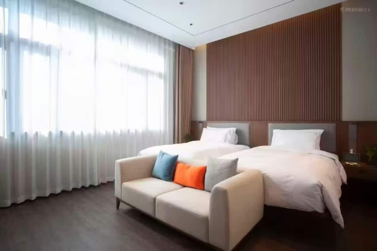 A hotel room with a bed, a sofa, and a large window with curtains.