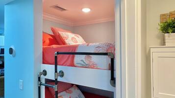 Ein Stockbett mit einem rot-weißen Musterdeckenbett, einer Metallleiter und einem kleinen Blumentopf auf einem Regal.