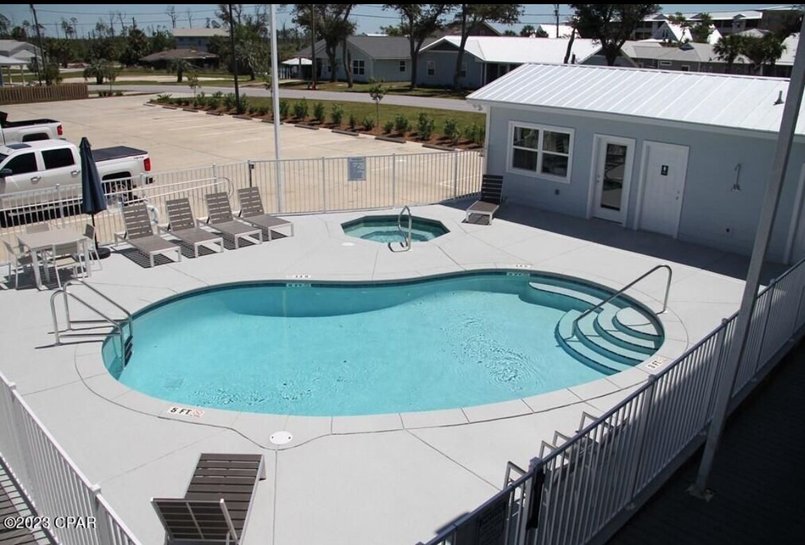 A swimming pool with a hot tub, lounge chairs, and a small building with a door and windows.