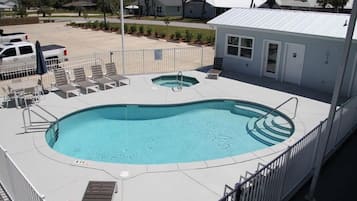A swimming pool with a hot tub, lounge chairs, and a small building with a door and windows.