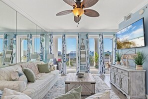 A spacious living room with a large sofa, a coffee table, and a TV mounted on the wall. - 2-bedroom waterfront condo with pool and hot tub in welcoming Mexico Beach (Mexico Beach)