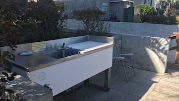 An outdoor kitchen area with a sink and countertop, surrounded by a concrete wall and some greenery.