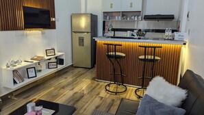 Una cocina compacta con refrigerador integrado, una zona de bar con taburetes y un espacio de descanso con sofá.