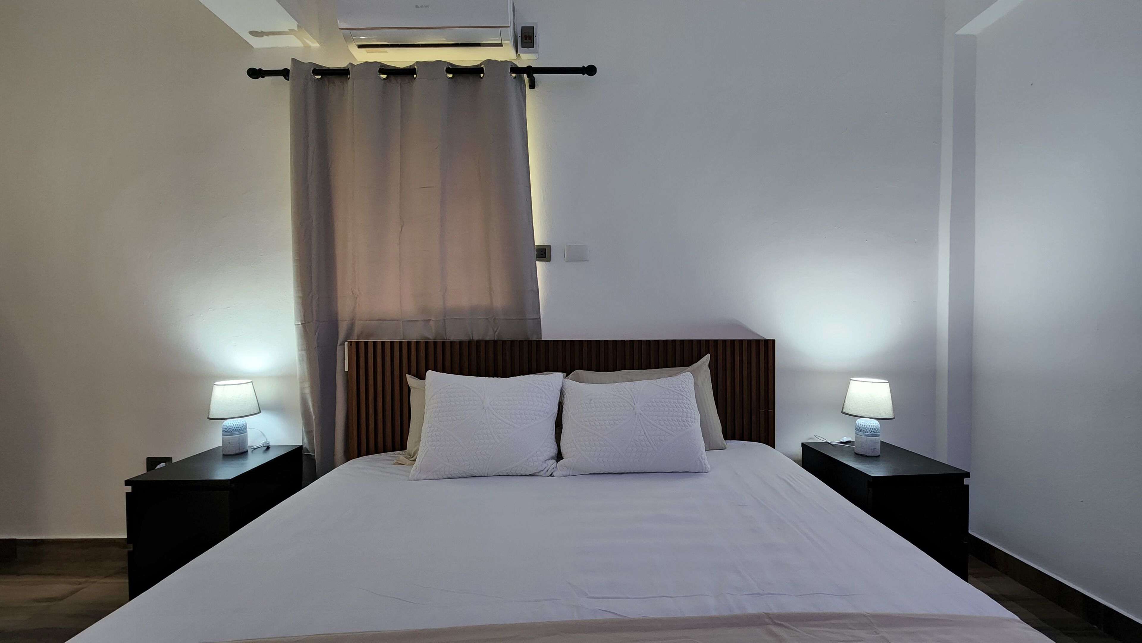 Ein Hotelzimmer mit einem großen Bett, zwei Nachttischen mit Lampen, einem hölzernen Kopfteil und einem Vorhang.