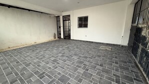 Una habitación con piso de baldosas, paredes blancas, un ventanal y una puerta con barrotes.