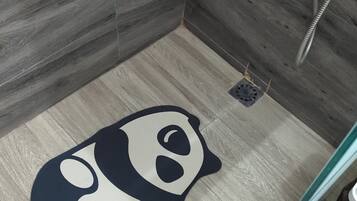 A bathroom with a shower area, a drain, and a panda-themed mat on the floor.