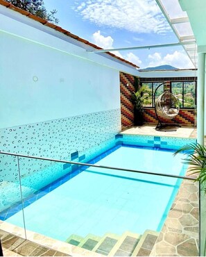 A swimming pool with clear blue water, surrounded by a white wall with a decorative pattern.