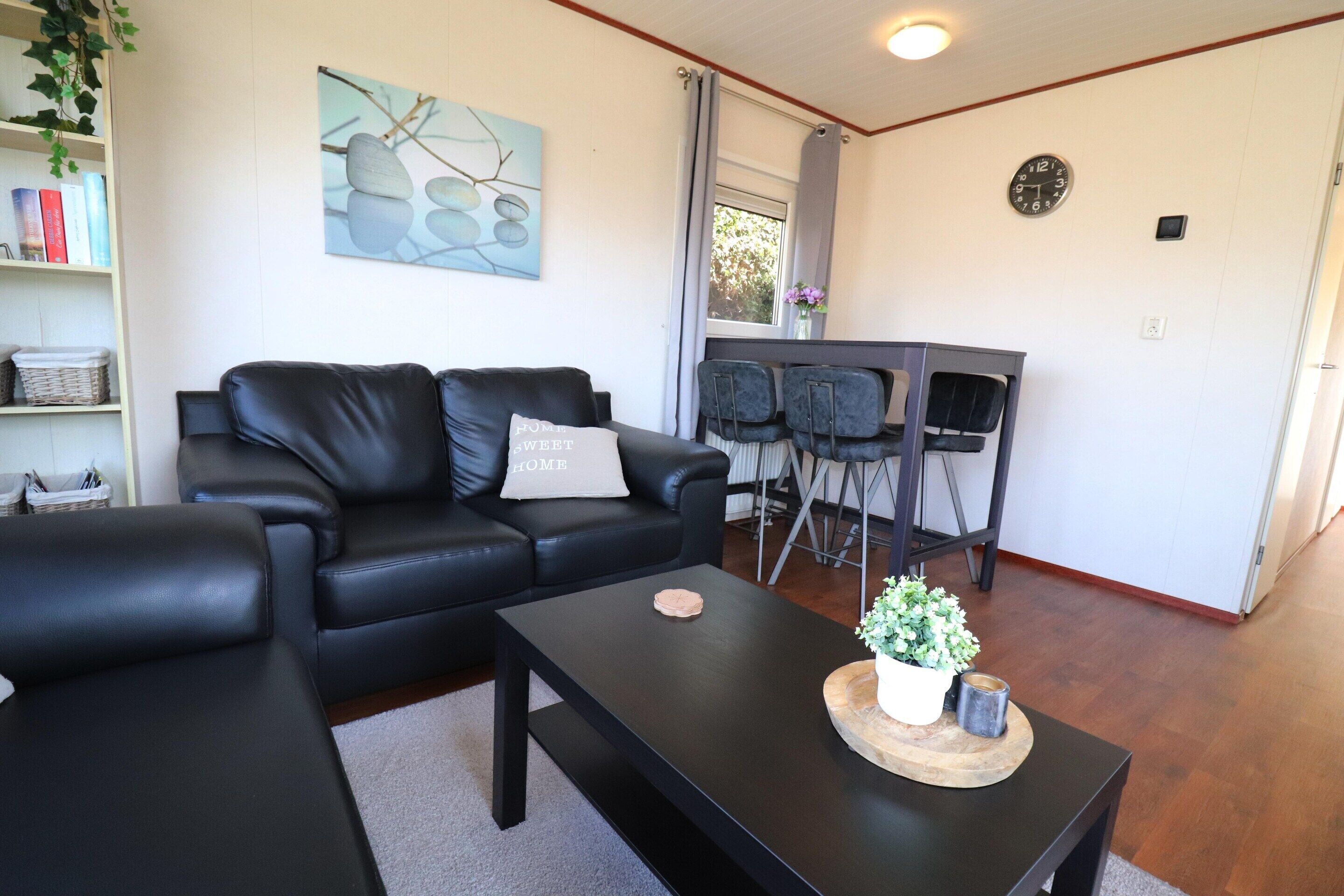 A modern living room with a black leather sofa, a coffee table, and a dining area with a chair.