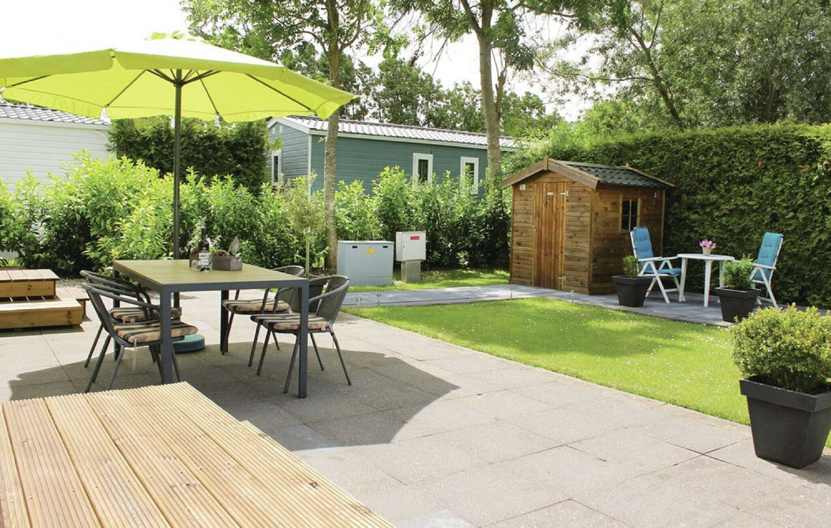 A patio area with a wooden table and chairs, a yellow umbrella, and a small wooden shed.