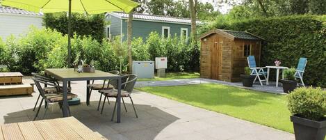 A patio area with a wooden table and chairs, a yellow umbrella, and a small wooden shed.