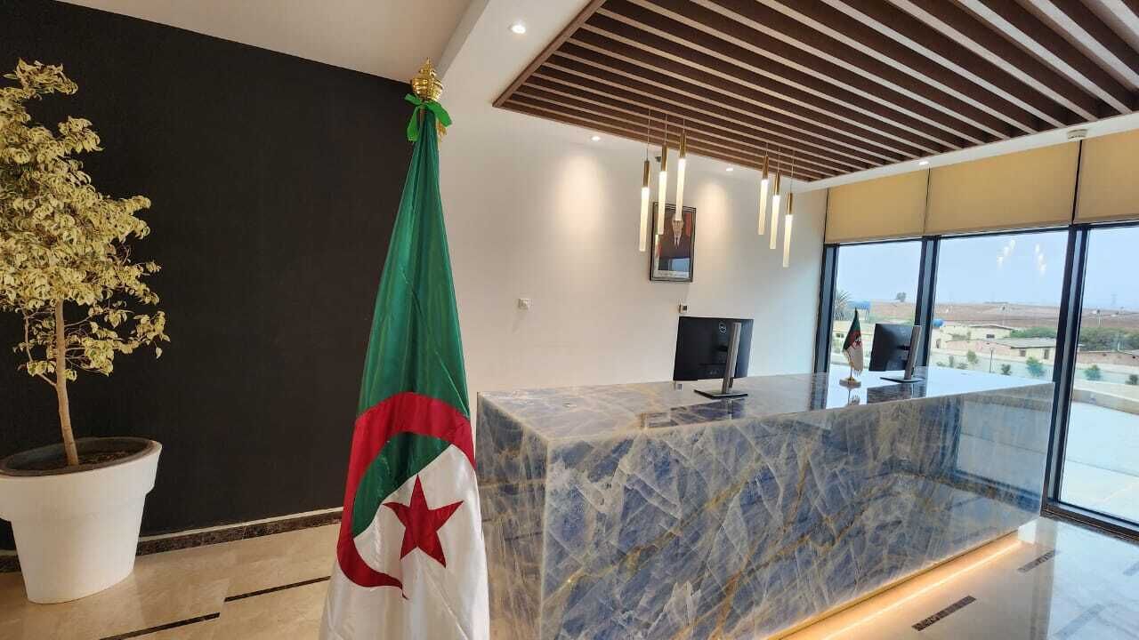 Un comptoir d’accueil moderne, doté d’un plateau en marbre, d’un drapeau et d’une plante en pot.