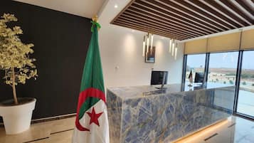 Un comptoir d’accueil moderne, doté d’un plateau en marbre, d’un drapeau et d’une plante en pot.