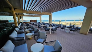 Un área de estar al aire libre techada con sillones y mesas, con vista a una playa.