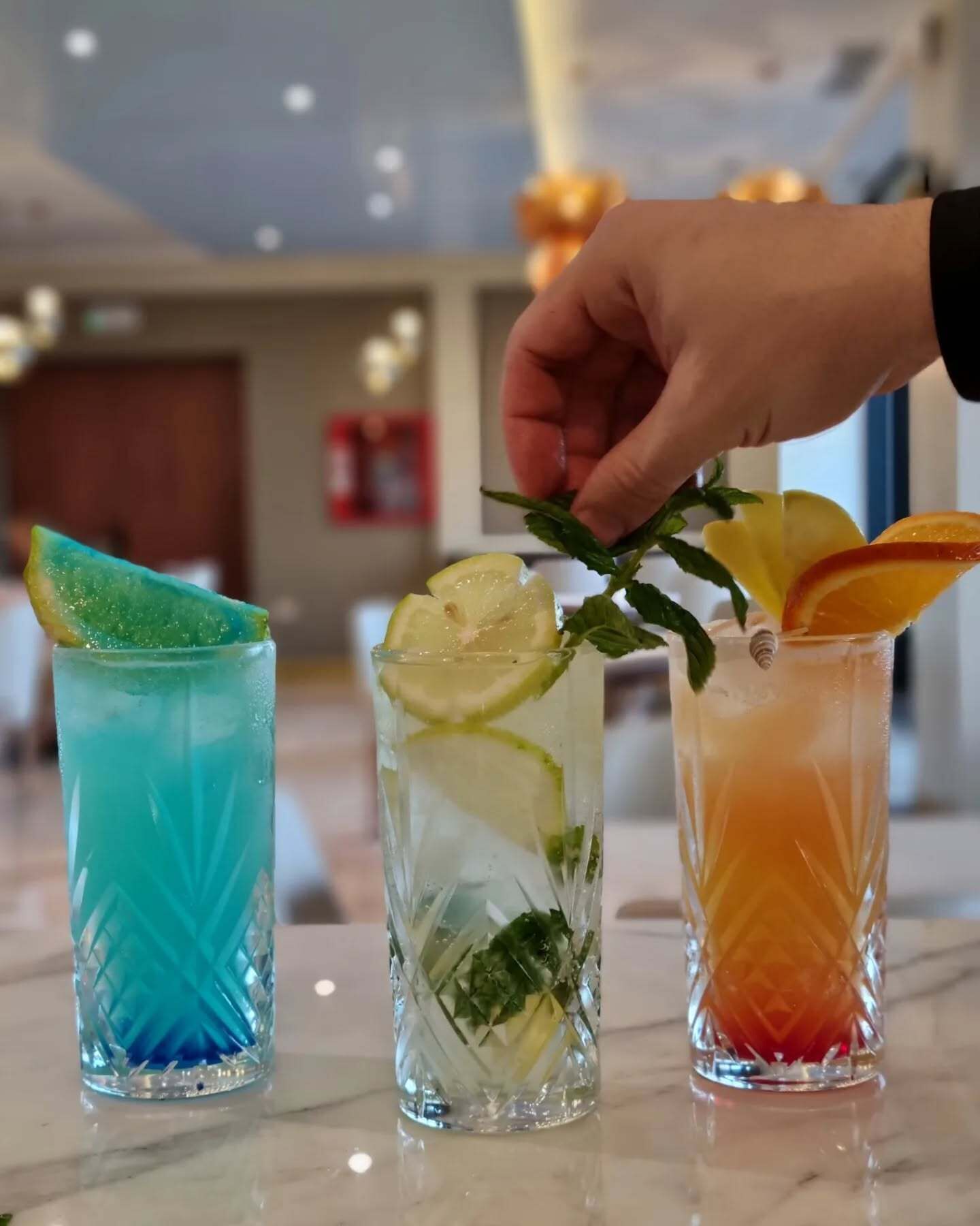 Three cocktails with lime slices and mint leaves, served in clear glasses on a marble countertop.