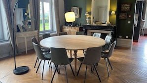 Un coin repas avec une table ronde en bois et six chaises, une cheminée et un grand miroir au mur.