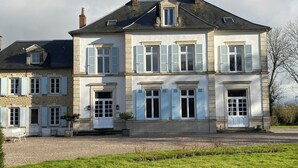 Un bâtiment à deux étages doté d’une façade symétrique, de nombreuses fenêtres avec volets et d’une allée gravillonnée.