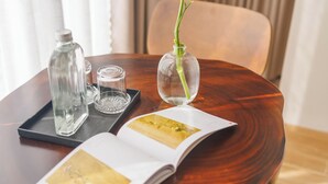 Uma mesa de madeira com um vaso contendo uma única flor amarela, uma garrafa de vidro e uma revista.