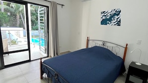 Un dormitorio con cama, ventilador de techo, ventana con vista a una piscina y unidad de aire acondicionado.