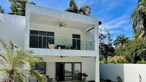 Una casa moderna de dos pisos con un balcón, un patio con mobiliario exterior y un césped bien cuidado.