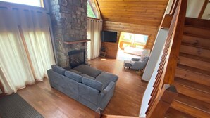 Una sala de estar acogedora con chimenea de piedra, un sofá gris y suelo de madera.