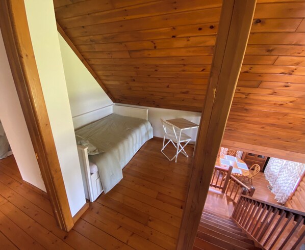 A small, cozy room with a wooden ceiling and floor, a single bed, a small table, and a chair.