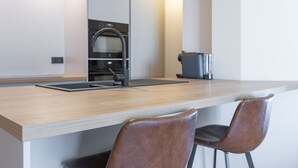 A modern kitchen with a wooden countertop, two brown leather chairs, a built-in oven, and a coffee machine. - Modern Studio With sea View (Middelkerke)