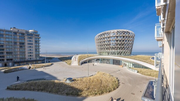 A modern building with a unique spherical structure, a flat-roofed building, and a sandy area with pathways. - Modern Studio With sea View (Middelkerke)