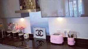 A modern kitchen with a black countertop, a pink toaster, a coffee maker, and a decorative item with a Chanel logo. - 1 Bed Apartment Sleeps 2 - Free Parking - (Dartford)