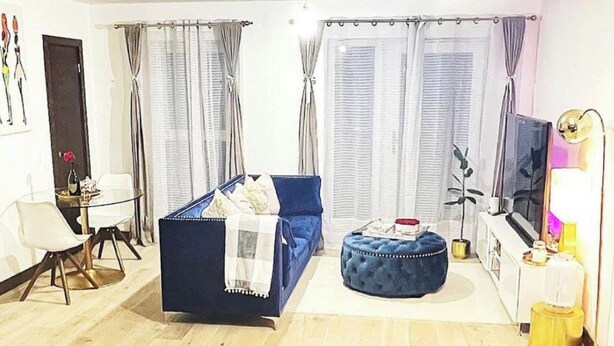 A living room with a sofa, ottoman, and a TV. There is a dining table with chairs, a plant, and a lamp. - 1 Bed Apartment Sleeps 2 - Free Parking - (Dartford)