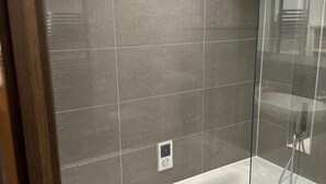 A bathroom with a glass shower enclosure, a white bathtub, and a small control panel on the wall. - 1 Bed Apartment Sleeps 2 - Free Parking - (Dartford)