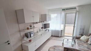 A modern living room with a sofa, a coffee table, and a TV. There is a small white stool and a rug on the floor. - Vacation apartment Storm am Holm (Schönberg)