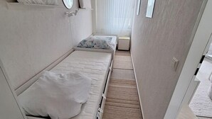 A small, narrow room with two beds, a mirror, and a window with sheer curtains. - Vacation apartment Storm am Holm (Schönberg)