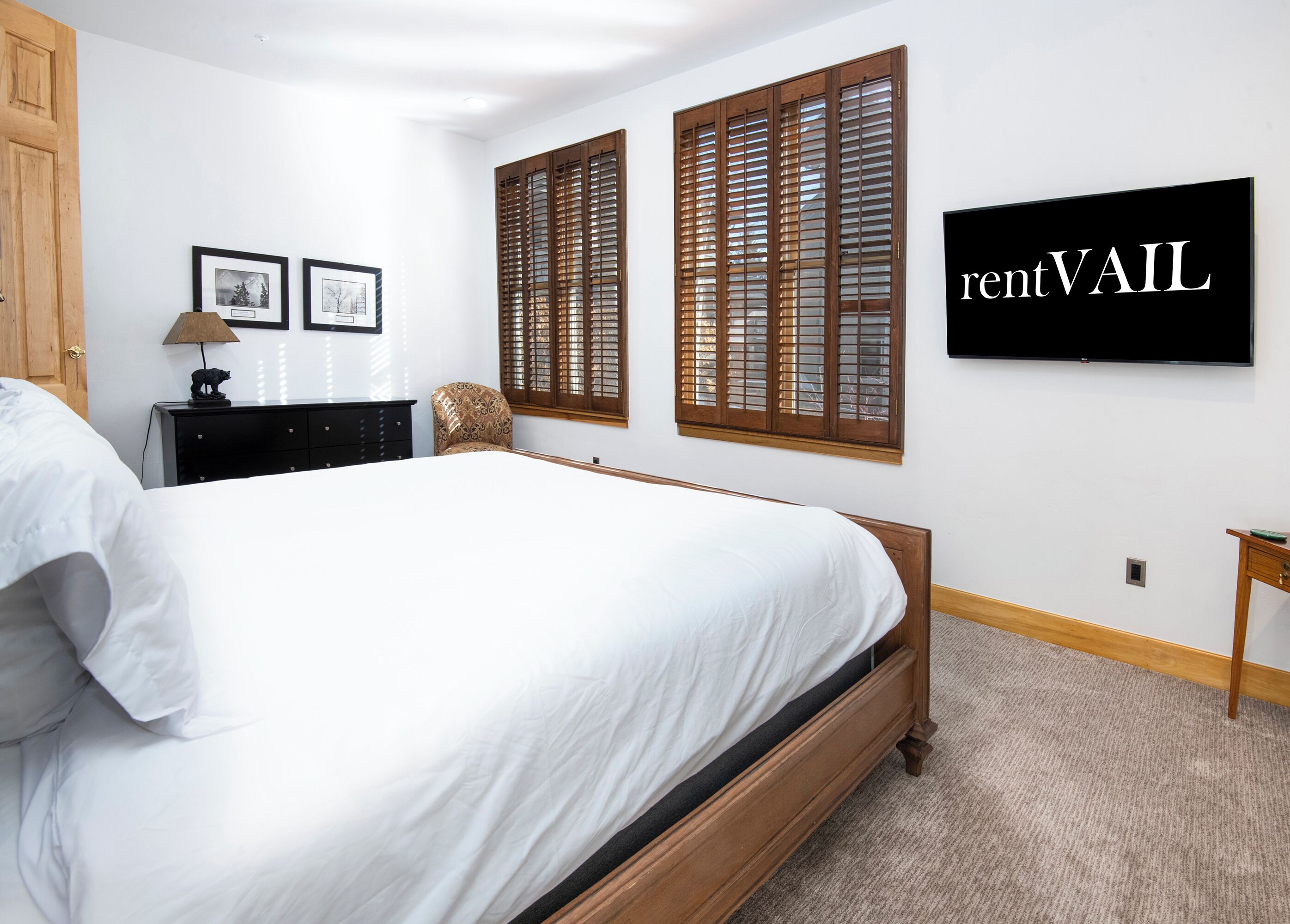 A bedroom with a large bed, wooden shutters, a flat-screen TV, and framed pictures on the wall.