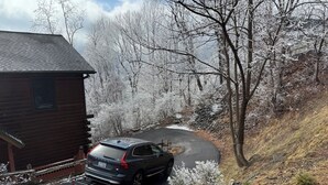 A cabin with a car parked in front, surrounded by snow-covered trees and a winding road. - THE LAZY BEAR, A luxury log cabin nestled in the heart of Maggie Valley. (Maggie Valley)