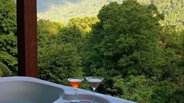 A hot tub with two martini glasses, surrounded by lush greenery. - THE LAZY BEAR, A luxury log cabin nestled in the heart of Maggie Valley. (Maggie Valley)