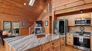 A spacious kitchen with wooden cabinetry, a marble countertop, and modern appliances including a refrigerator, microwave, and stove. - THE LAZY BEAR, A luxury log cabin nestled in the heart of Maggie Valley. (Maggie Valley)