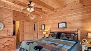 A wooden cabin bedroom with a bed, a dresser, a ceiling fan, and framed pictures on the wall. - THE LAZY BEAR, A luxury log cabin nestled in the heart of Maggie Valley. (Maggie Valley)