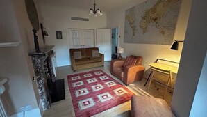 A cozy living room with a red patterned rug, a brown sofa, a leather armchair, and a map on the wall.