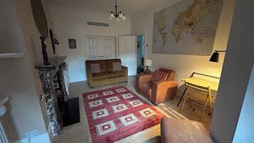 A cozy living room with a red patterned rug, a brown sofa, a leather armchair, and a map on the wall.