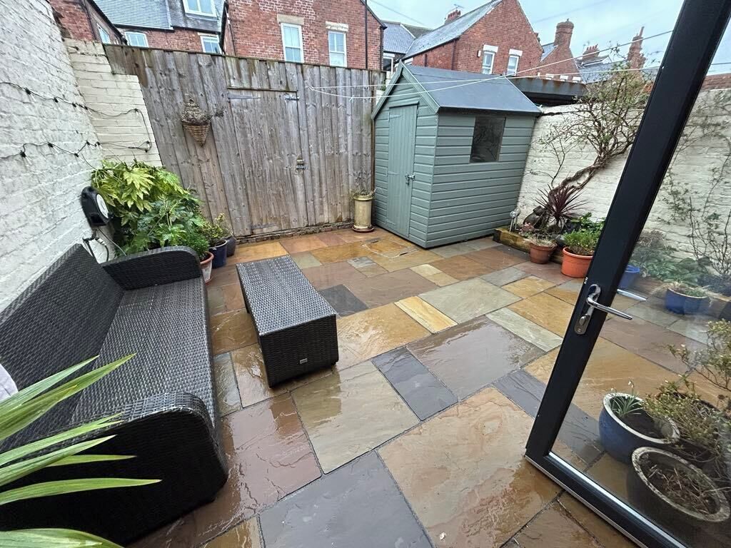 A patio with a wooden fence, a small shed, and potted plants.