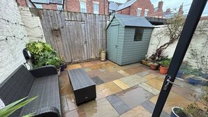 A patio with a wooden fence, a small shed, and potted plants.