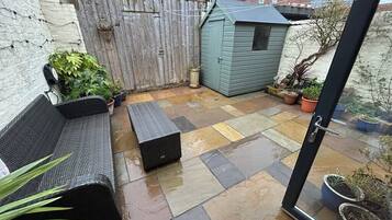 A patio with a wooden fence, a small shed, and potted plants.
