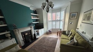 A living room with a fireplace, green sofas, a television, and a bookshelf.
