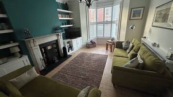 A living room with a fireplace, green sofas, a television, and a bookshelf.