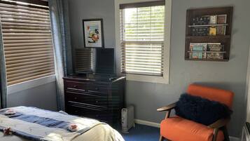 Een slaapkamer met een bed, dressoir, televisie, ramen en een boekenkast.