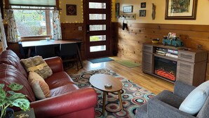 A cozy living room with a leather sofa, a grey armchair, a small round table, and a fireplace. There is a wooden wall with framed pictures and a door with a window. - Artist/Writer retreat- fab breakfast! (Corvallis)