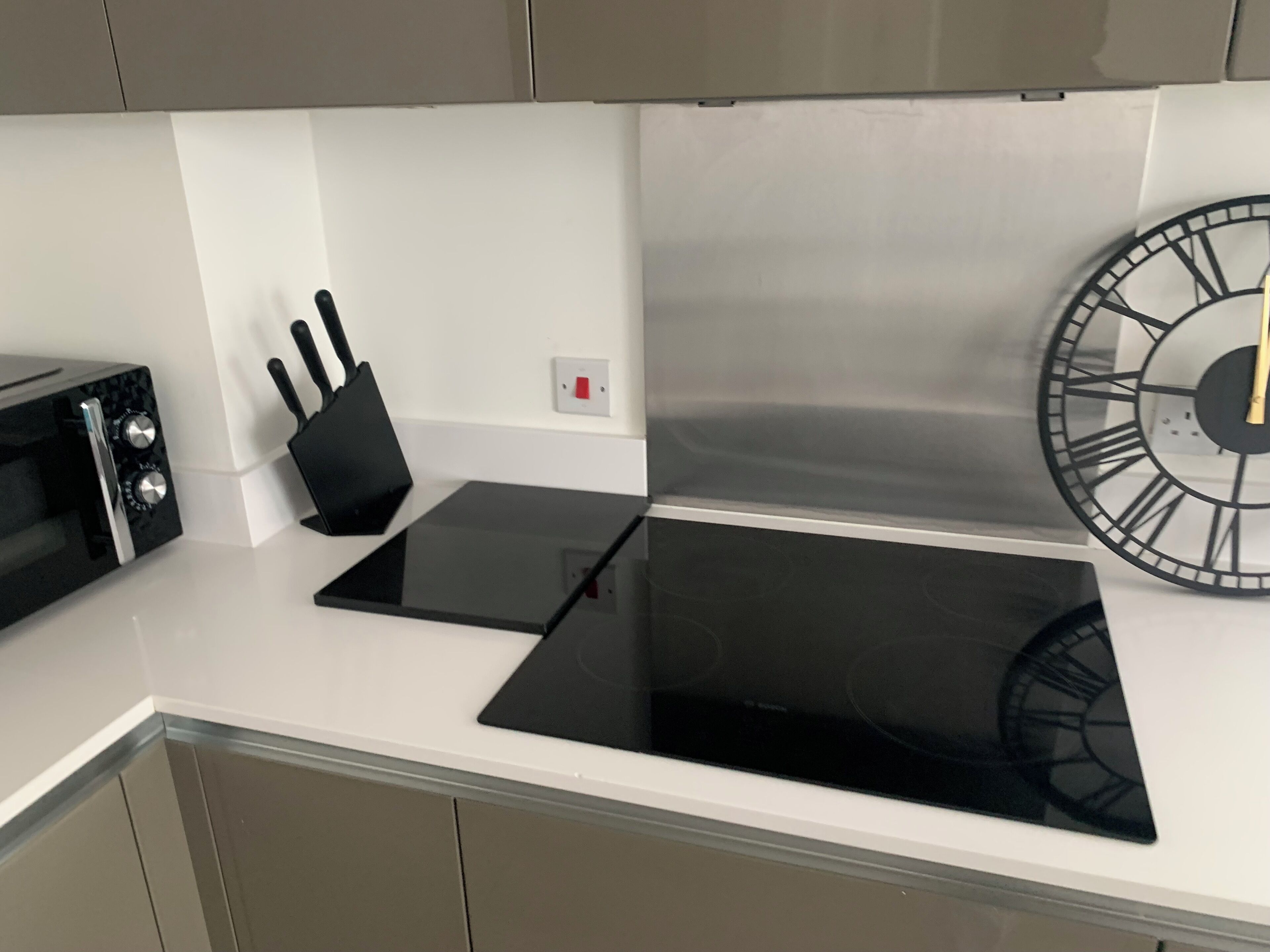 A kitchen with a black induction cooktop, a toaster, and a wall clock.